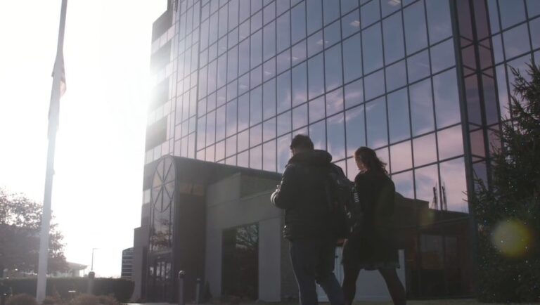 Two people wearing Baker Newman Noyes backpacks walking by a large office building